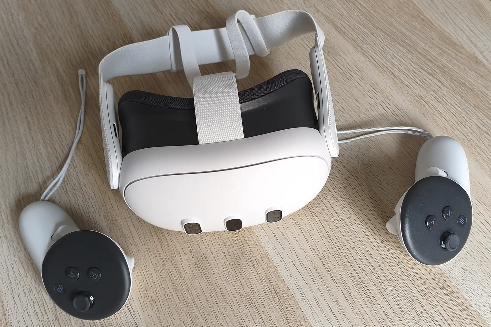 Gafas de realidad virtual Meta Quest 3 blancas y sus dos mandos sobre una mesa de madera.