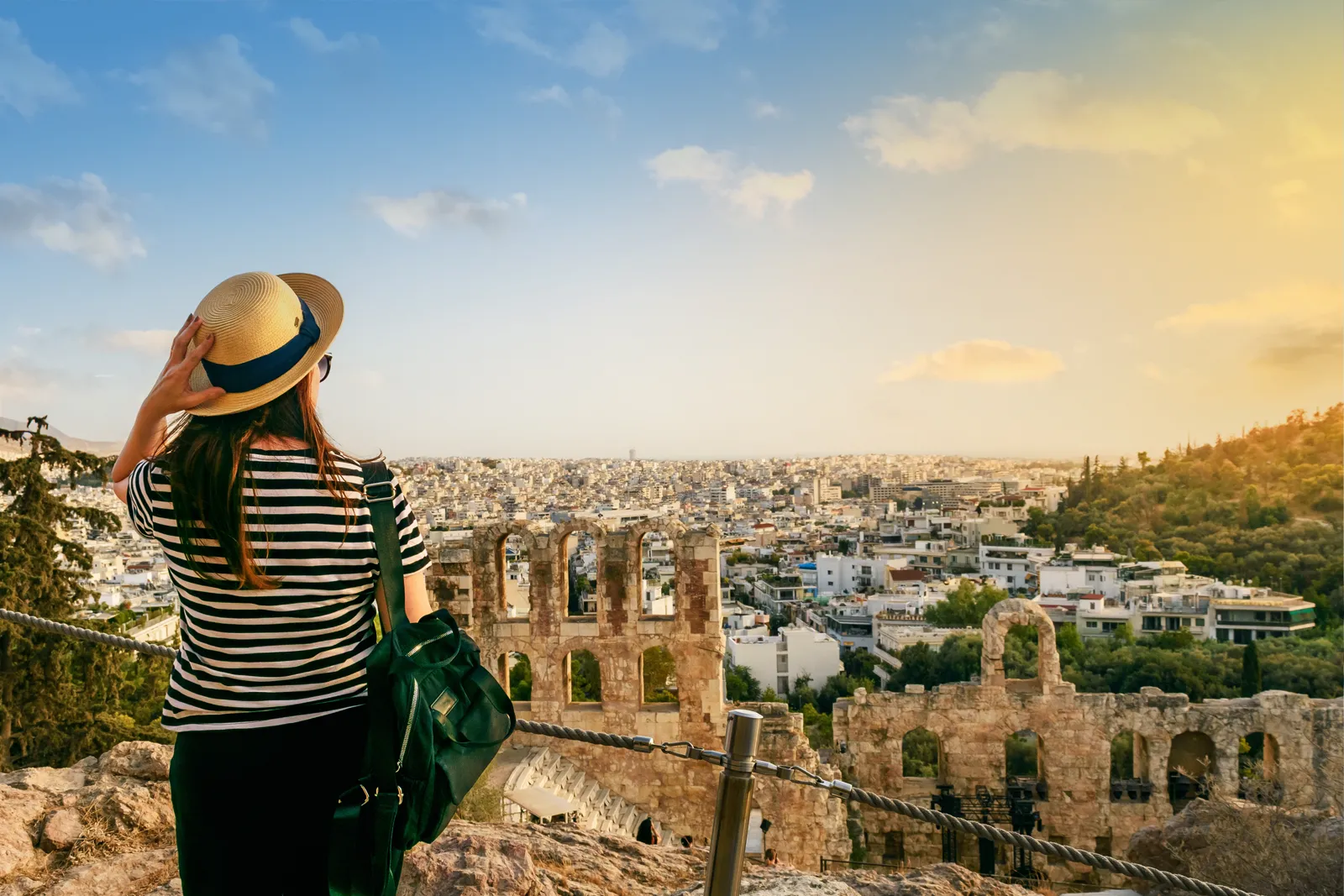 Mujer de espaldas con sombrero y mochila contemplando una ciudad desde un mirador