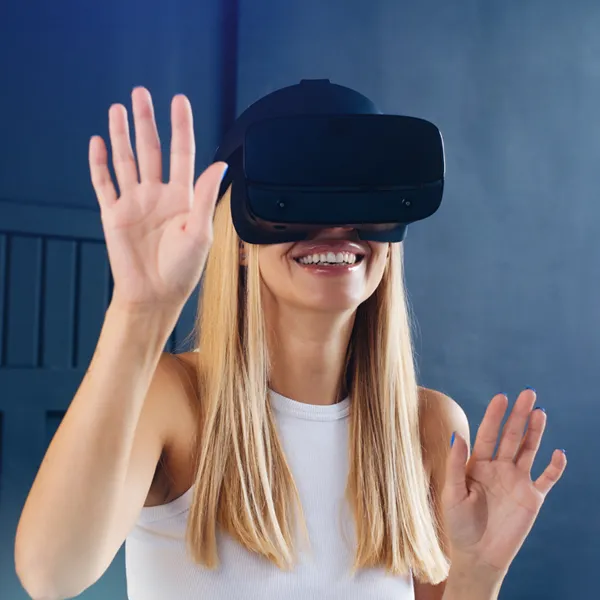 Mujer sonriendo con gafas de realidad virtual y las manos levantadas, sobre un fondo azul.