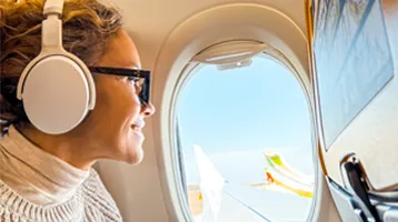 Mujer con auriculares mirando por la ventanilla de un avión